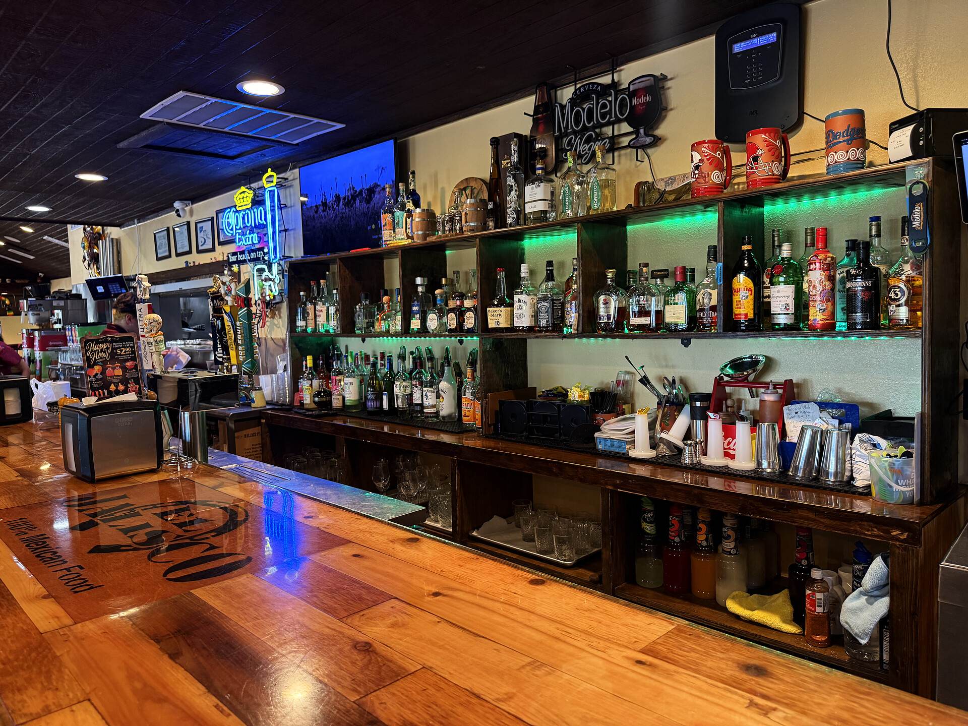 The back bar at El Jalisco #3, bottles ranked on the shelves under green light