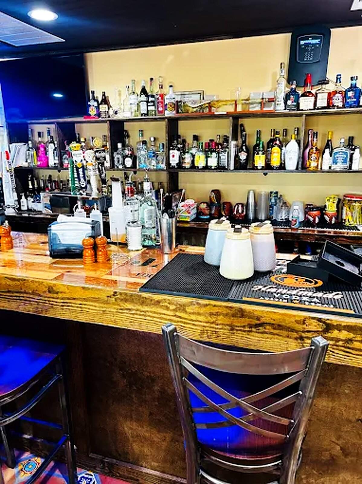 The full bar at El Jalisco #3 — bottles backlit on the shelves above the counter
