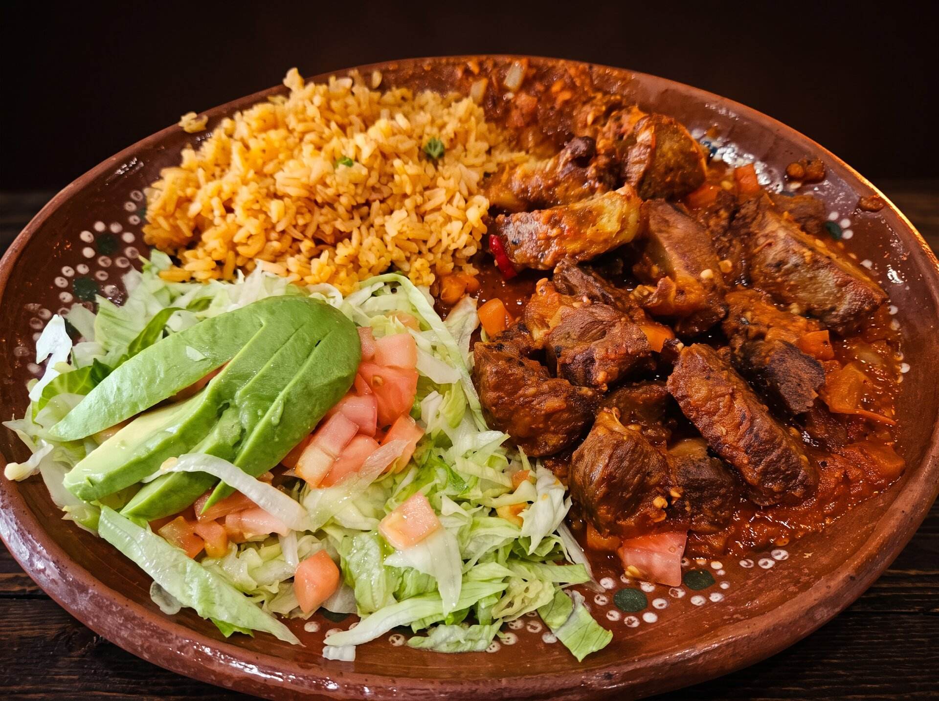 Carne guisada with Spanish rice, avocado and salad on a clay plate