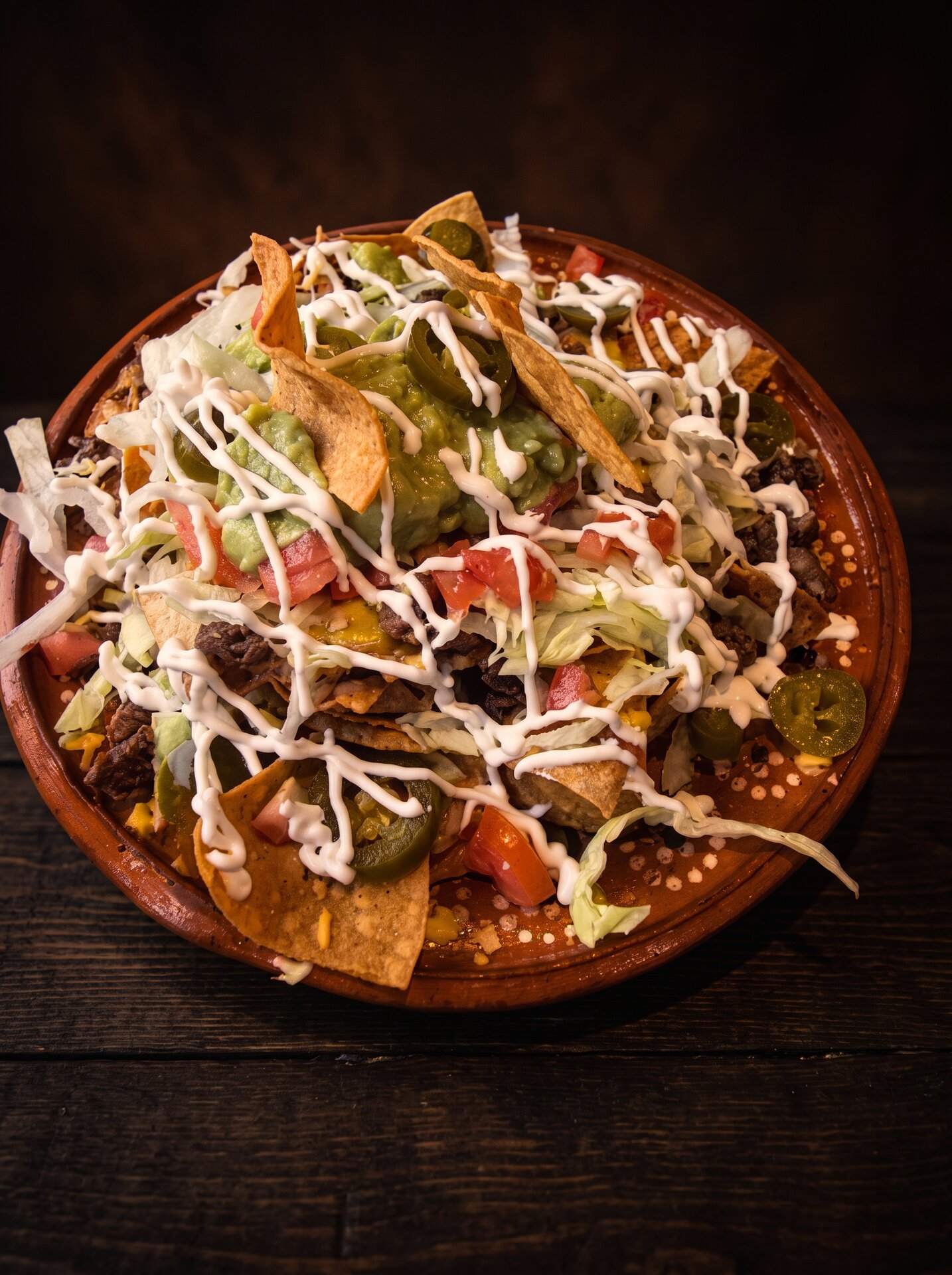 Chilaquiles in red sauce under shredded cheese, crema and sliced jalapeño
