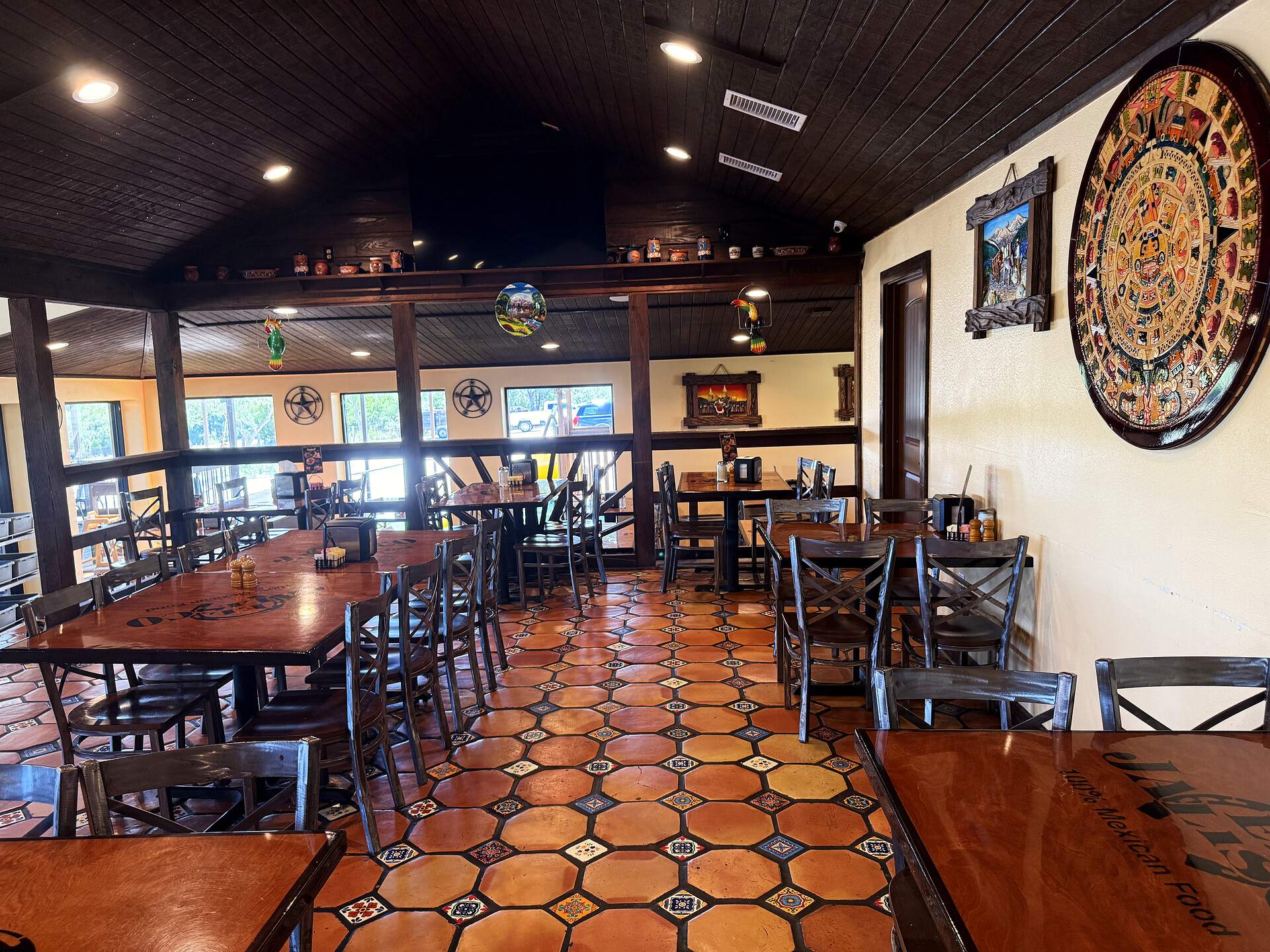 A dining room at El Jalisco #3 — tables on Saltillo tile beneath a carved Aztec sun stone on the wall