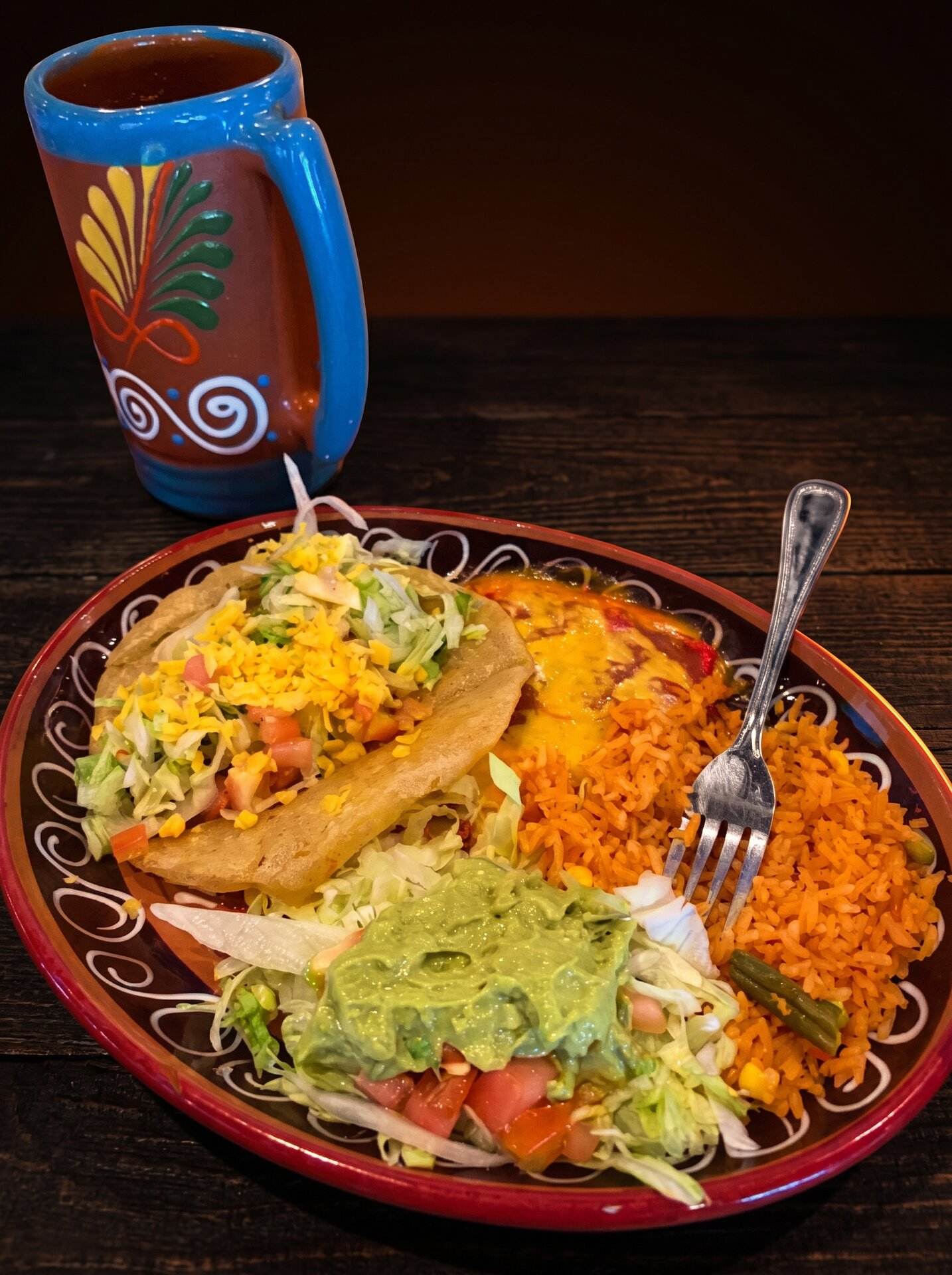 Two enchiladas with rice, guacamole and salad on a red clay plate