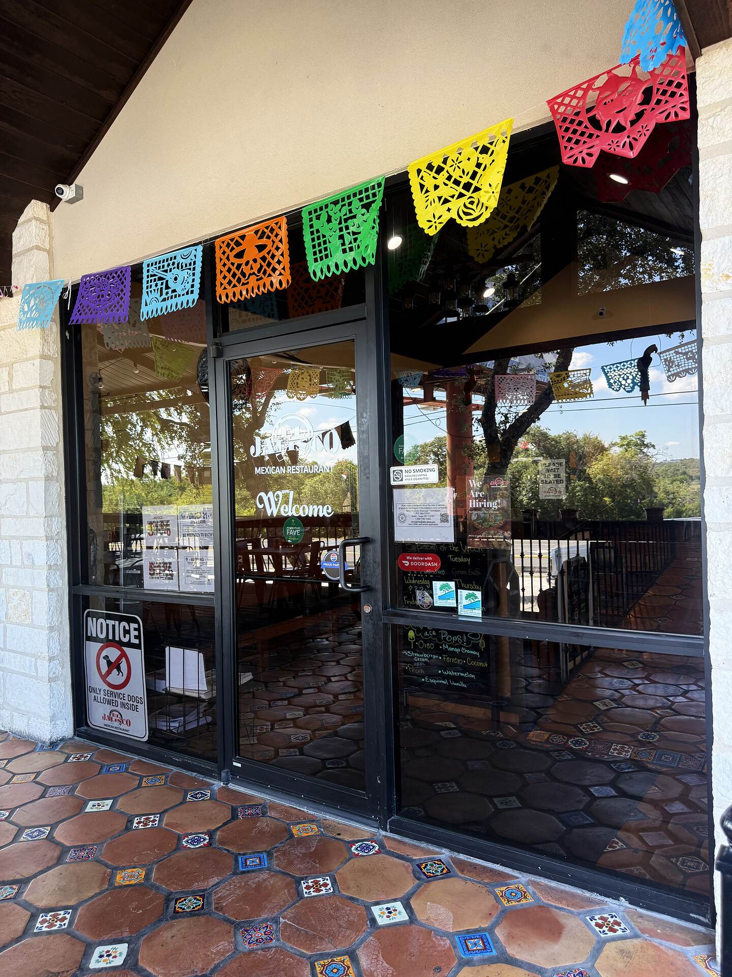The entrance at El Jalisco #3 — glass doors under strings of papel picado, on a Saltillo tile floor
