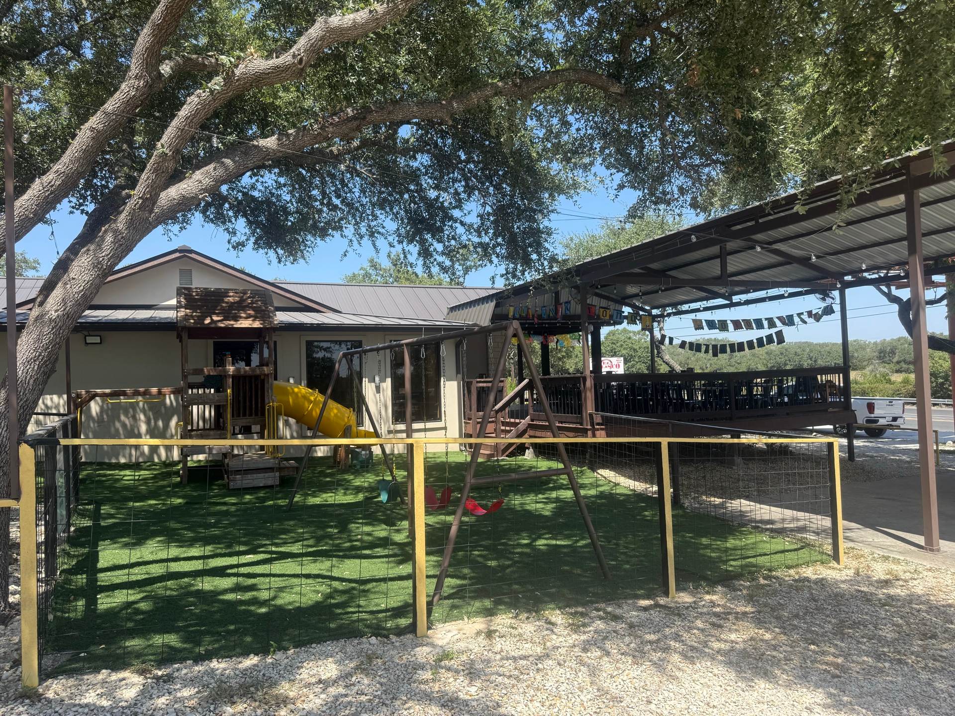The playground under a live oak, the covered patio and its papel picado just beyond