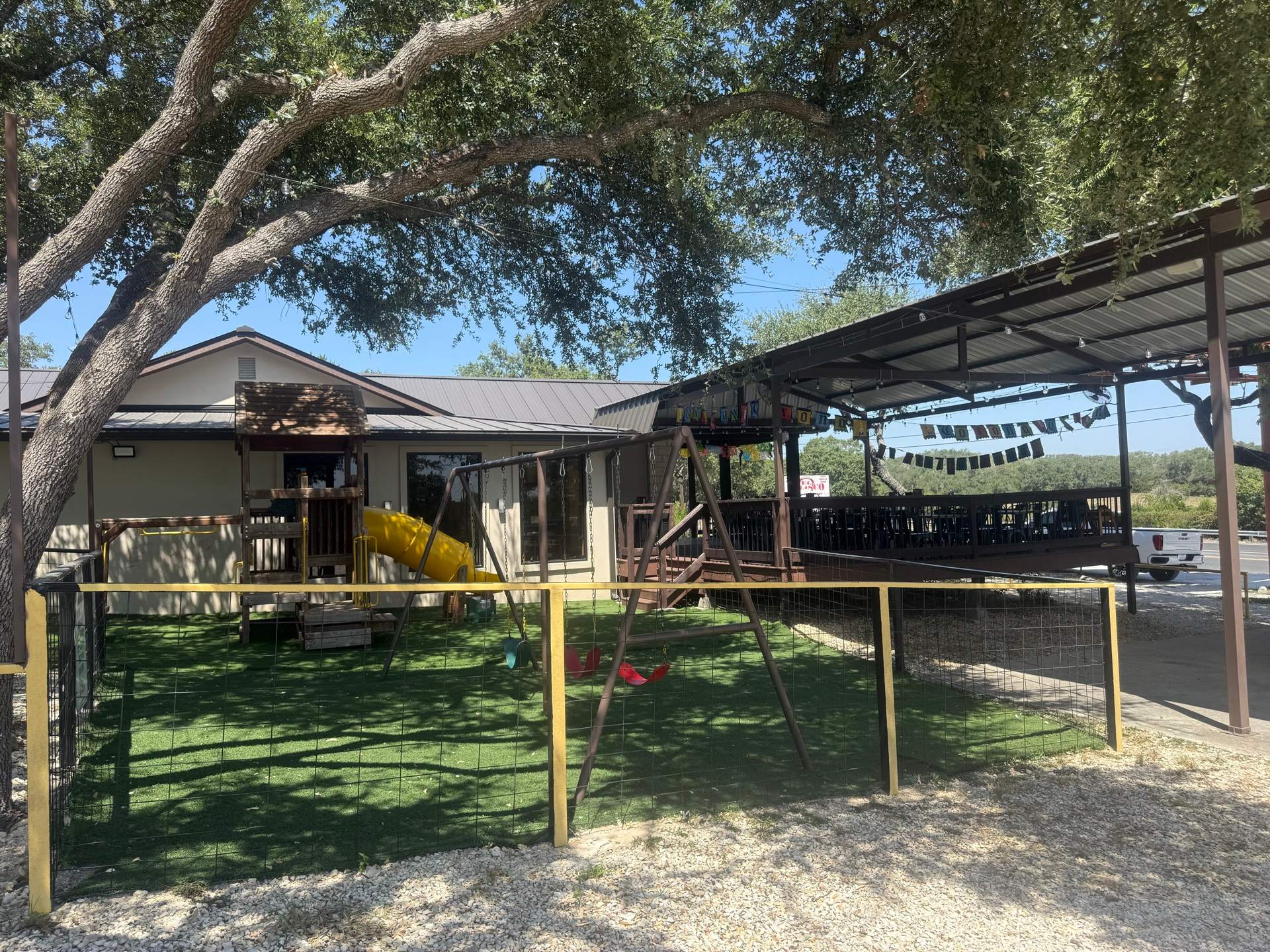 The playground under a live oak, the covered patio and its papel picado just beyond