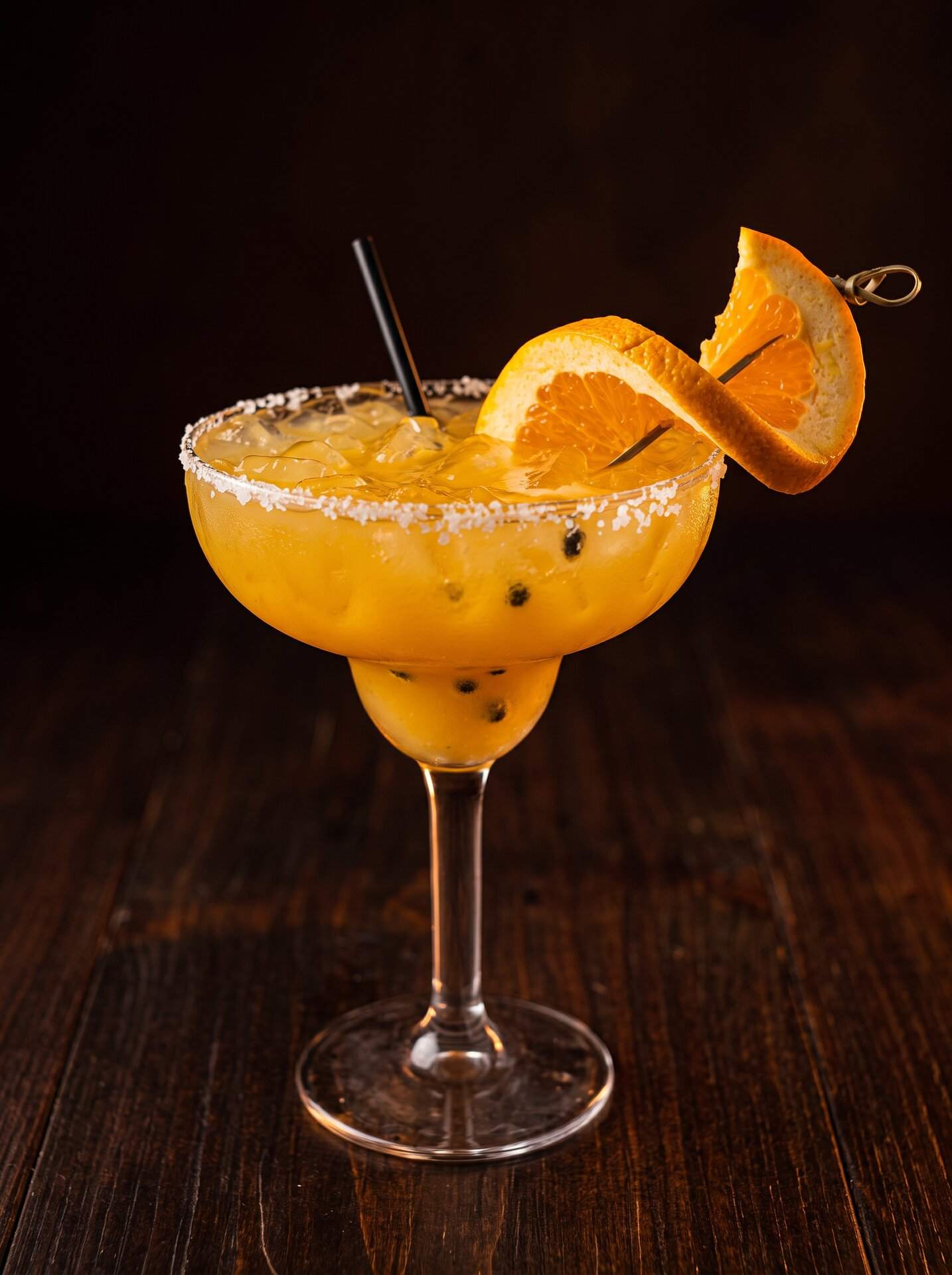 A mango margarita in a salt-rimmed coupe with an orange wheel