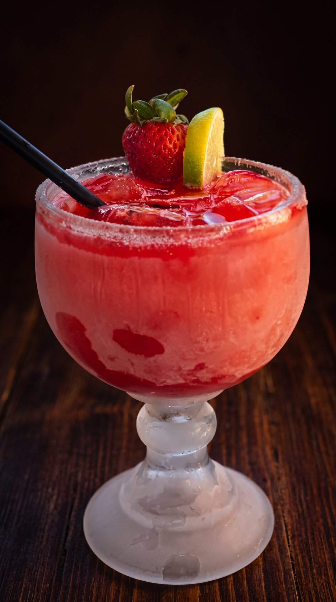 A frozen strawberry margarita in a goblet, topped with a whole strawberry and lemon