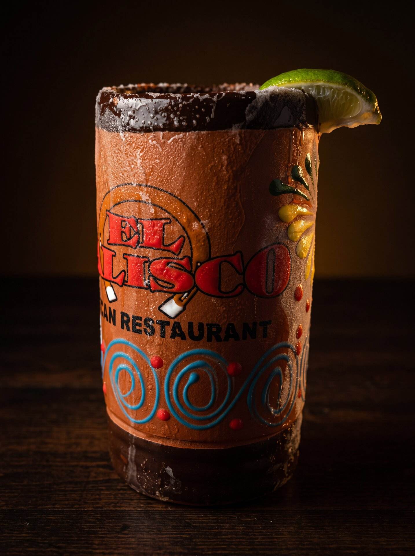 A michelada in the branded El Jalisco clay mug with a chile rim and lime