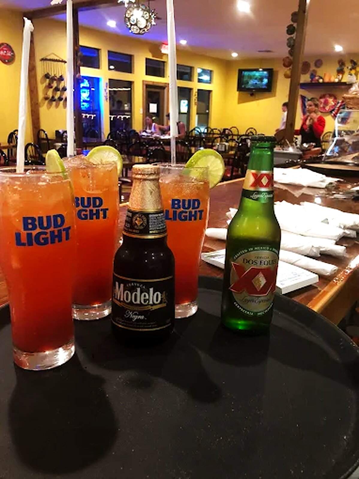 Two micheladas at the bar beside bottles of Bud Light, Modelo and a Mexican lager