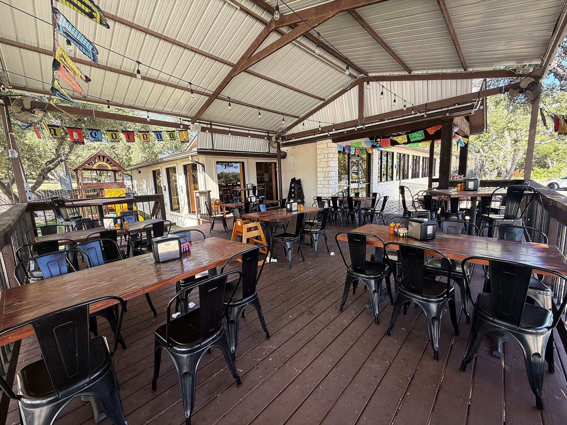 The covered patio set for service — rows of wooden tables and metal chairs, open to the trees on every side