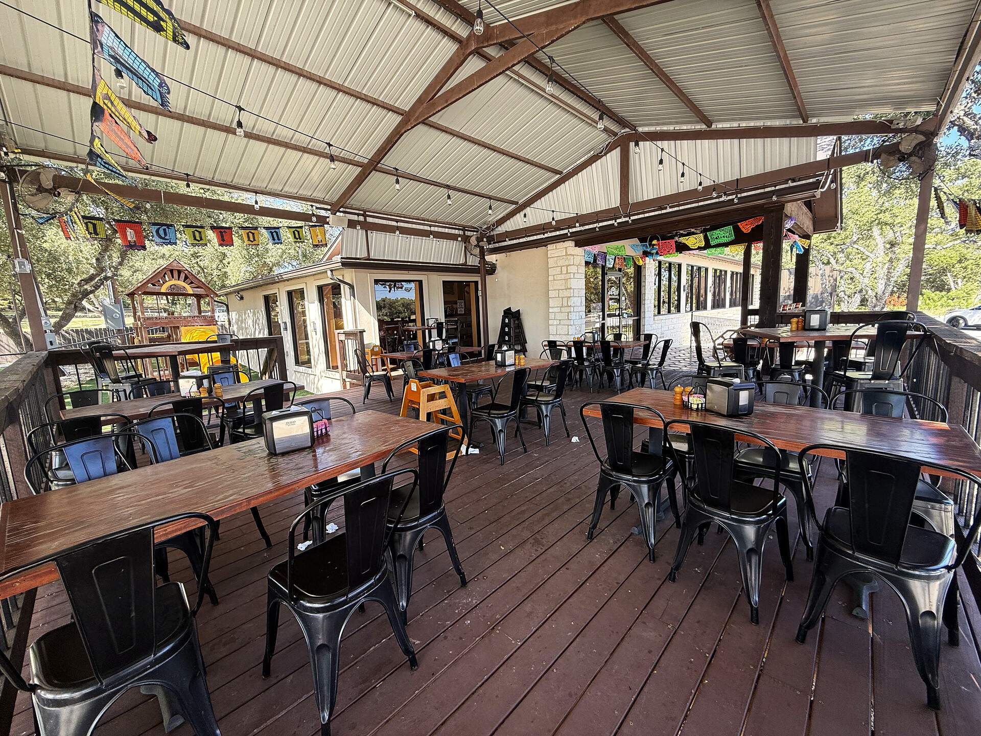 The covered patio set for service — rows of wooden tables and metal chairs, open to the trees on every side