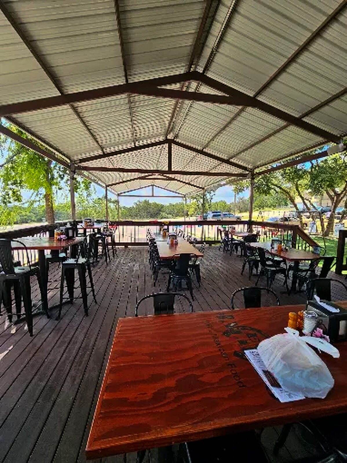 The covered patio deck with metal roof, long wooden tables and the Hill Country beyond