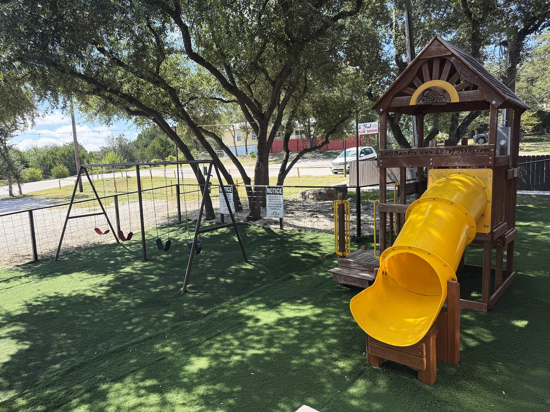 The playground behind the restaurant — a wooden play tower with a yellow tube slide and swings under the live oaks