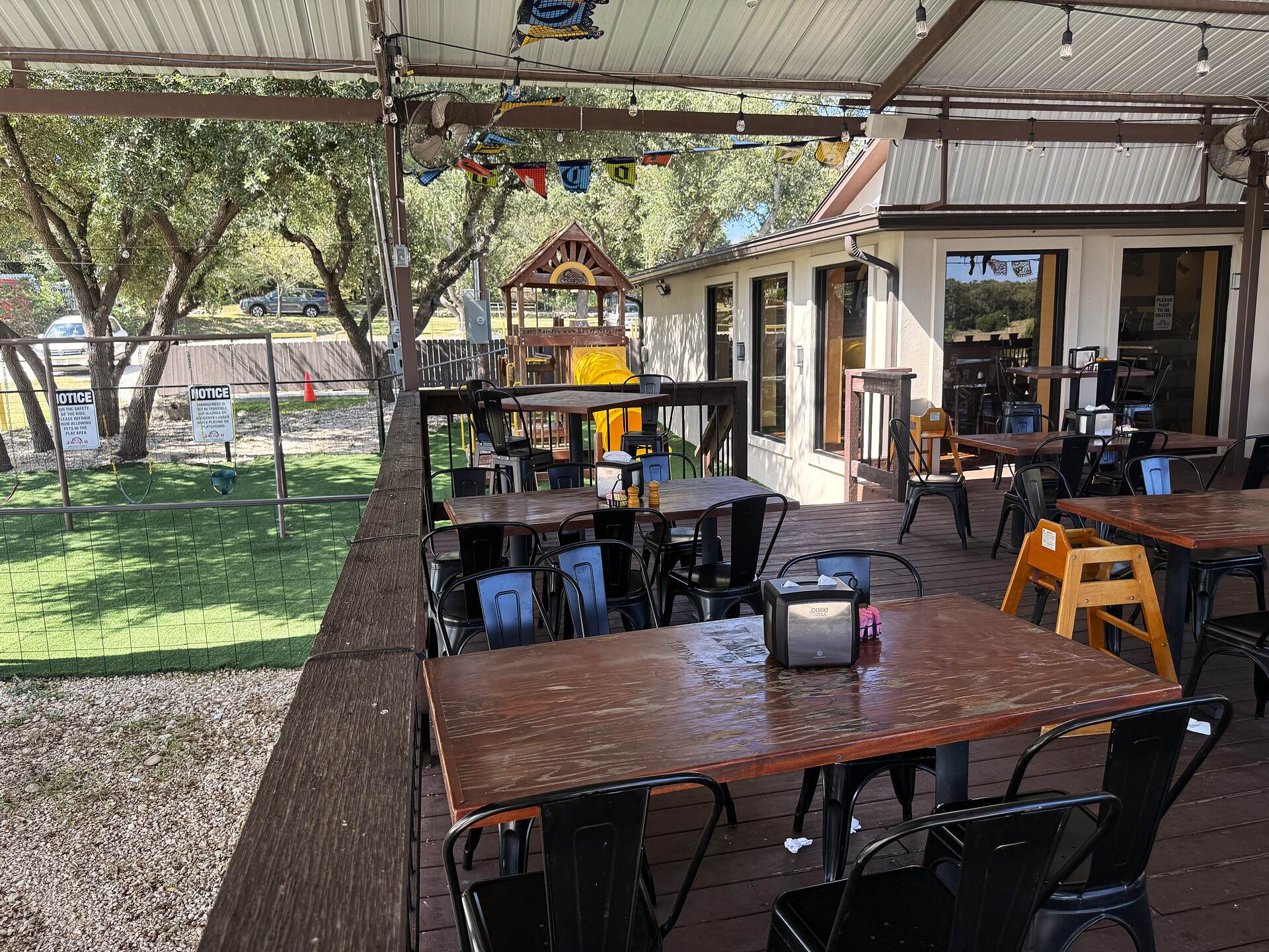 Patio tables beside the lawn, strung lights overhead and the restaurant behind
