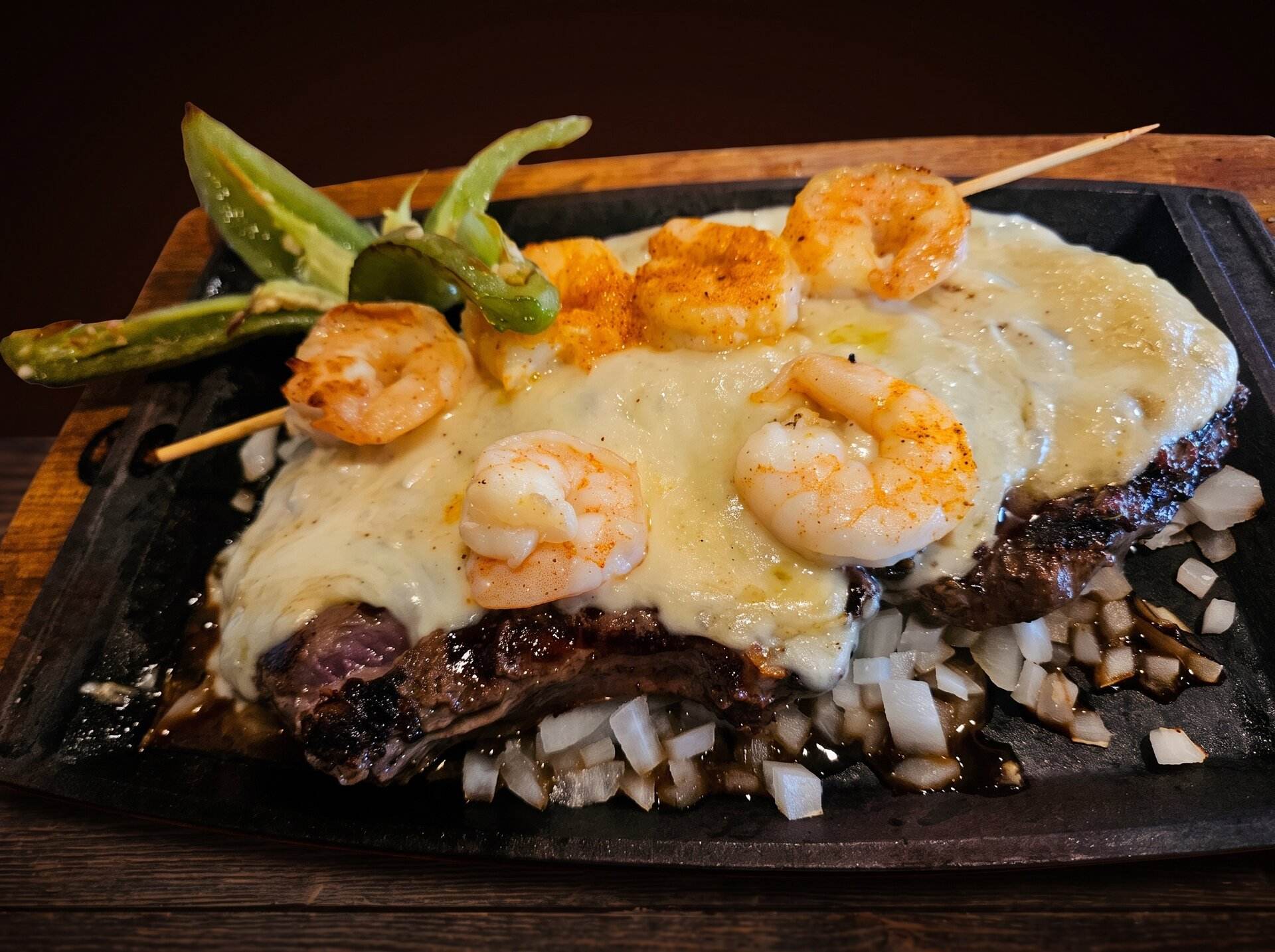 Steak flameado on a sizzling plate under melted cheese, topped with shrimp and grilled chiles