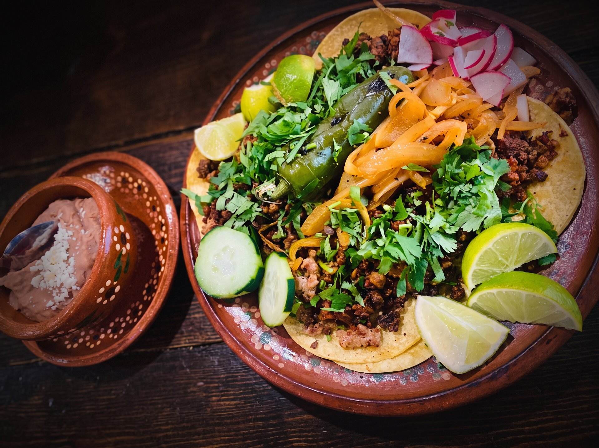 Street tacos garnished with radish, cucumber and lime beside a bowl of salsa