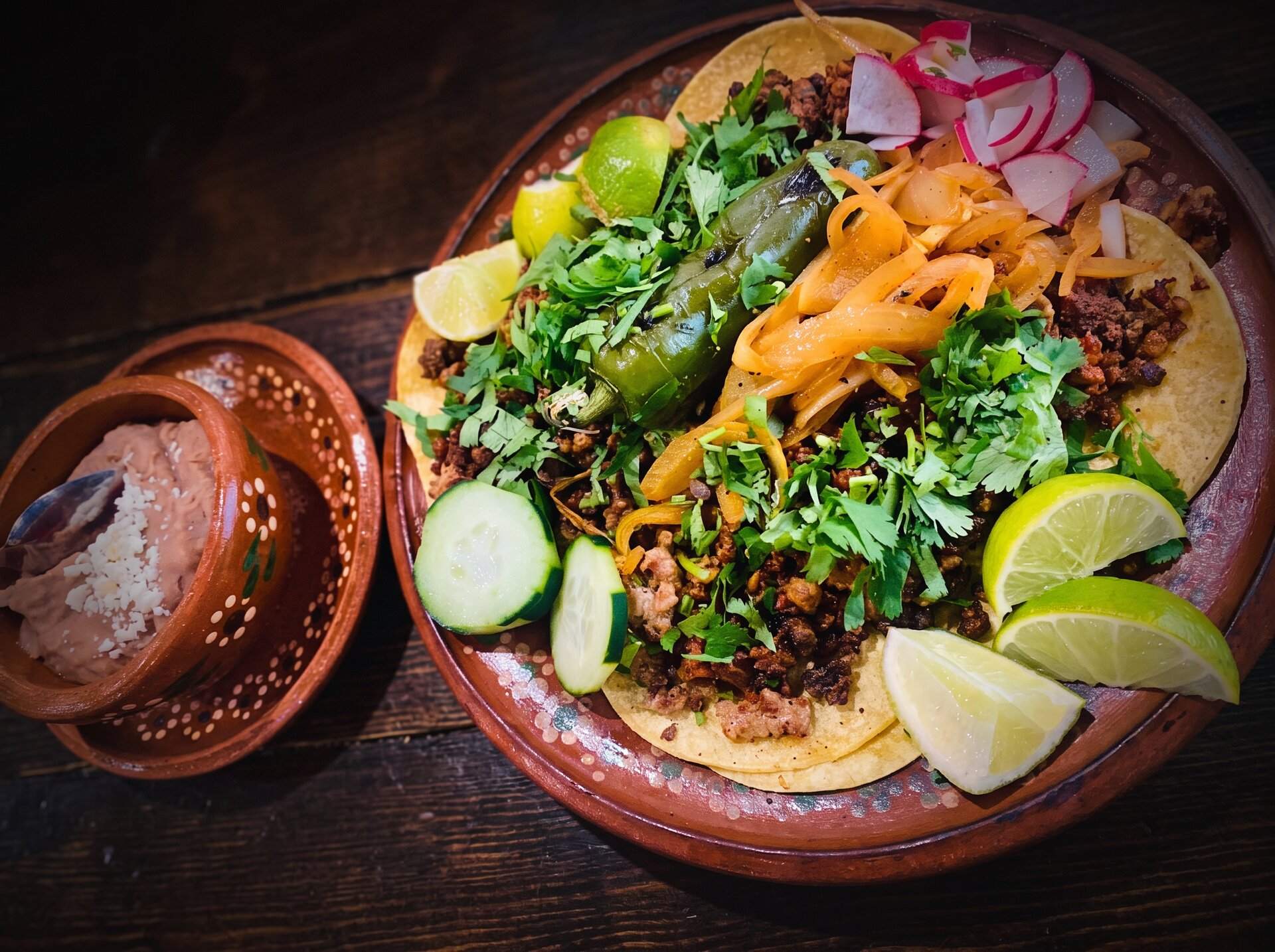 Street tacos garnished with radish, cucumber and lime beside a bowl of salsa