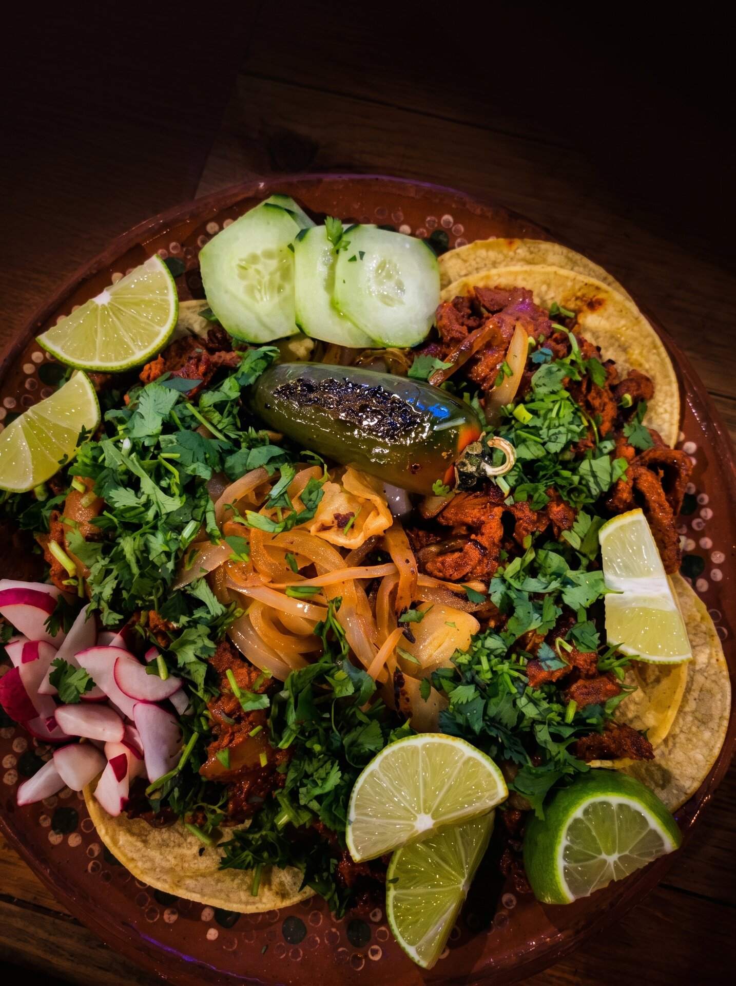 Overhead view of tacos ringed with lime, radish, cilantro and a roasted jalapeño