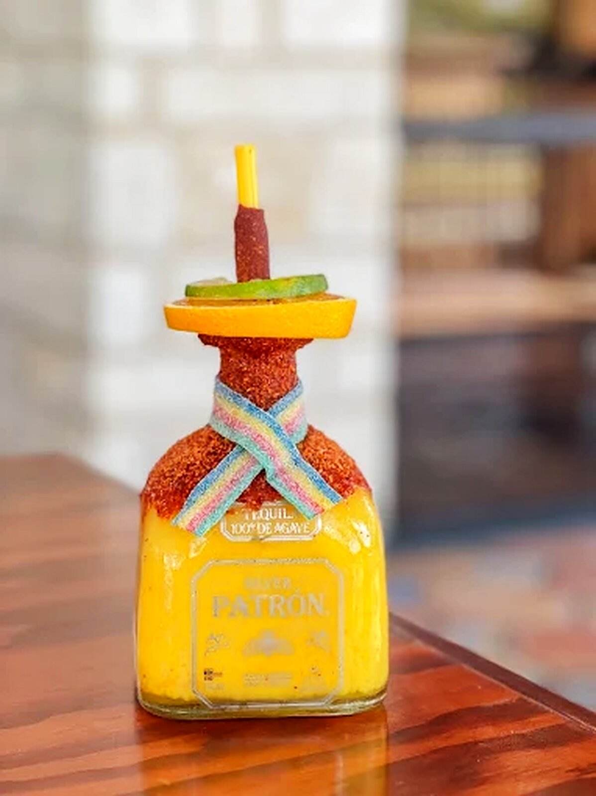 A Patrón tequila bottle dressed with a chile rim and citrus, on the bar top